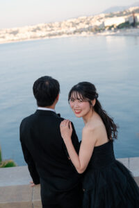 ニースの海辺で新郎の肩に手を置き微笑む花嫁のポートレート