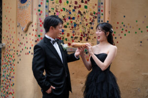 ニースのカラフルな壁の前でフランスパンを見つめる新郎新婦