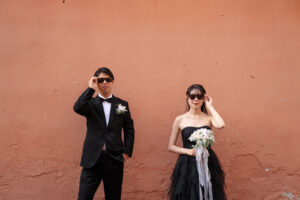 ニースのパステルカラーの壁を背景に、サングラスをかけてポーズをする新郎新婦