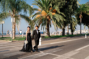 ニースの海岸線のヤシの木を背景に横断歩道を渡る新郎新婦