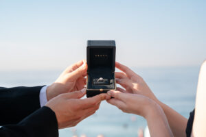 ニースの海とGRAFFの婚約指輪の箱を持つカップルの手