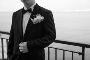 ニースの海を背景にポーズを決める新郎のアクセサリーにクローズアップしたモノクロ写真